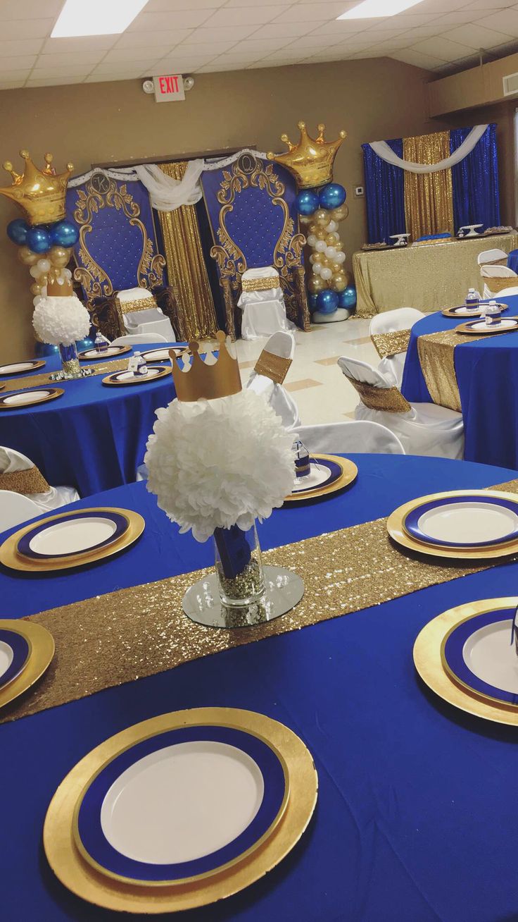 a table set up for a party with blue and gold plates, napkins, and centerpieces