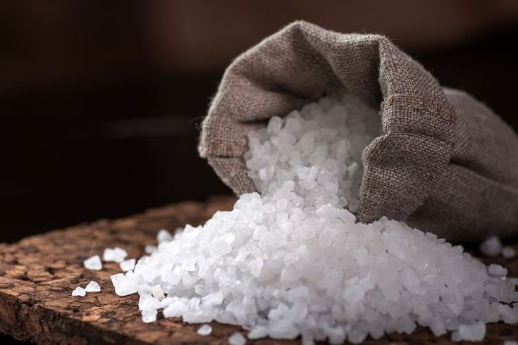 a sack filled with white sugar sitting on top of a wooden table next to a pile of rice