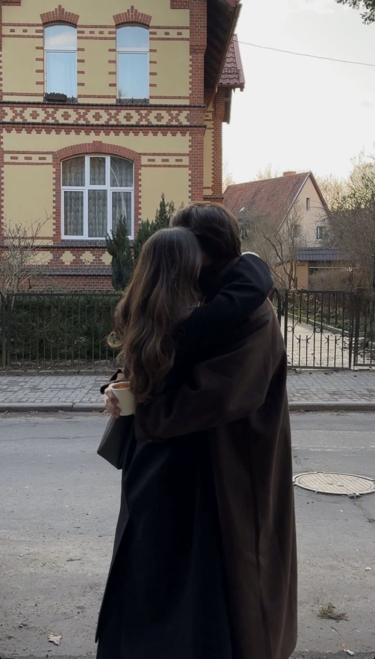 a man and woman hugging in front of a large brown house with white trim on the windows