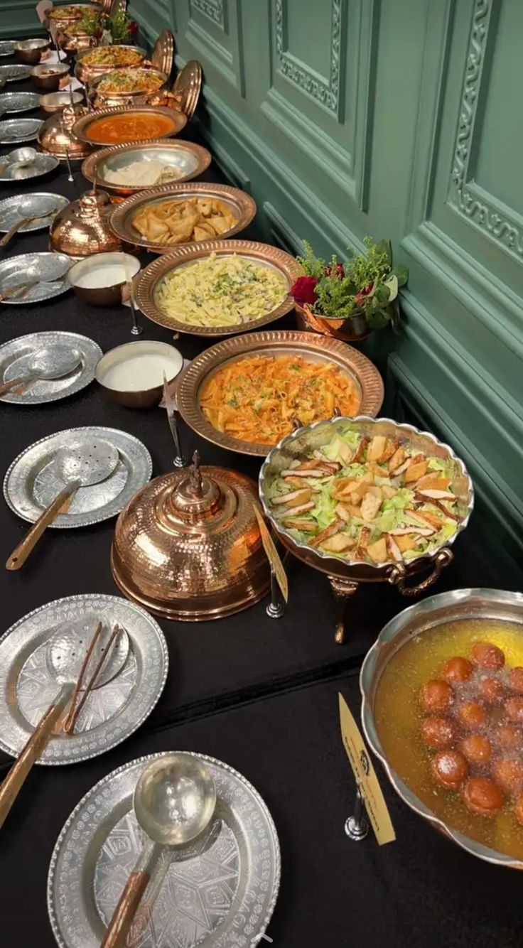 a long table filled with lots of different types of food and silver plates on top of it