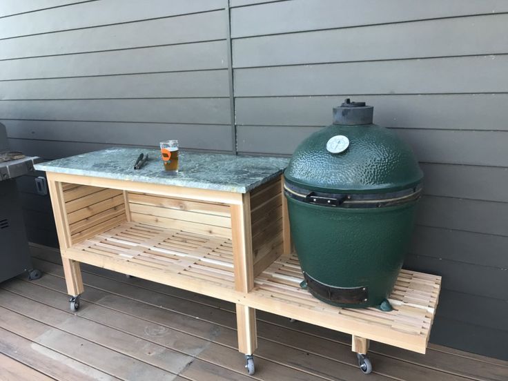 a big green egg sitting on top of a wooden table next to a bbq