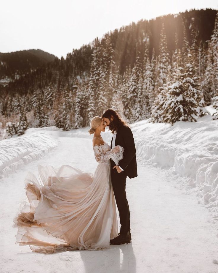 a bride and groom are standing in the snow with their arms around each other as they kiss