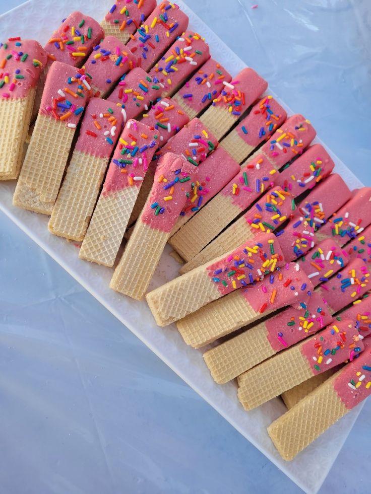 ice cream sticks with sprinkles and pink frosting are arranged on a plastic tray