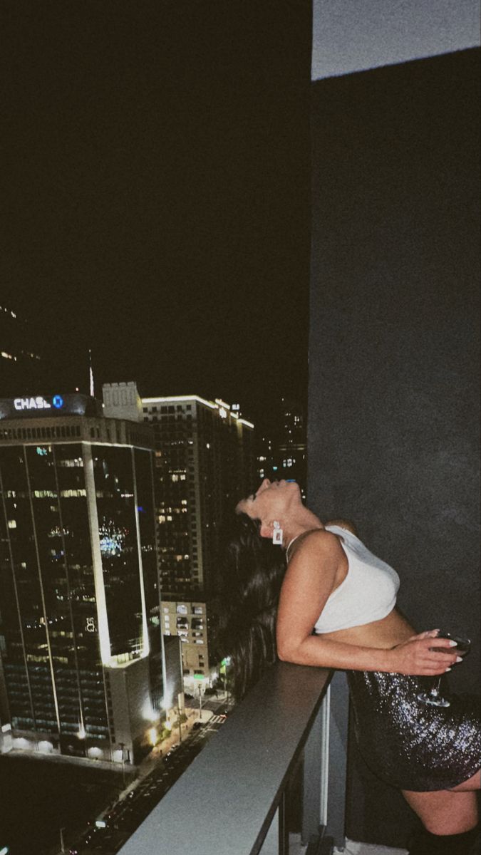 a woman standing on top of a balcony next to a tall building in the city