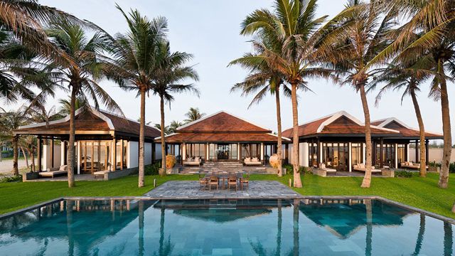 an outdoor swimming pool surrounded by palm trees and lounge chairs in front of the house