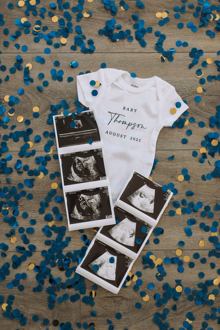 some blue and gold confetti next to a baby's bodysuit on a wooden floor