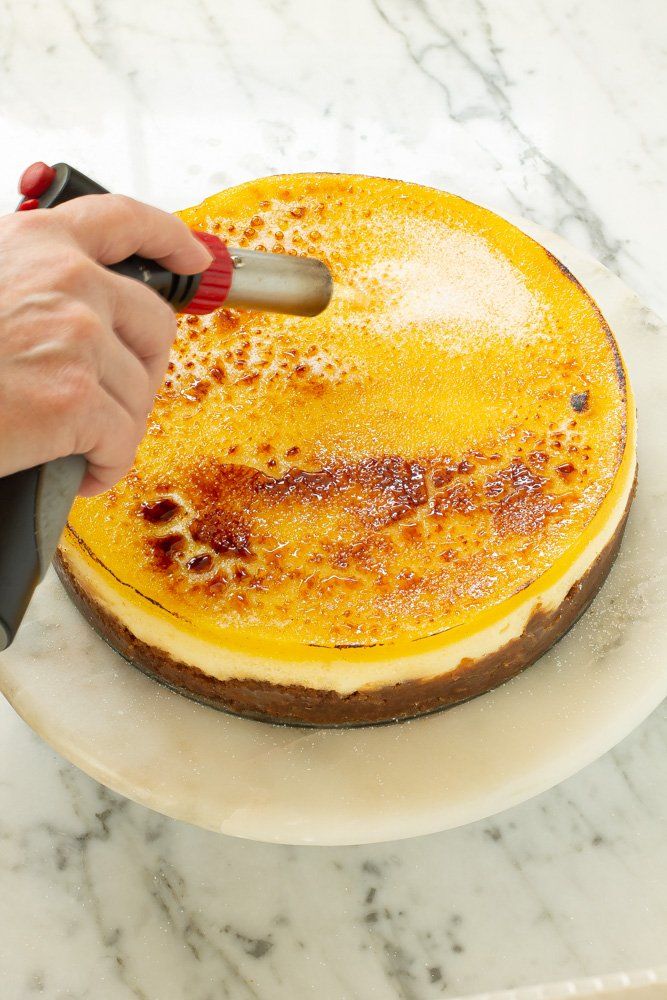 a person using a knife to cut into a cheesecake on a white platter