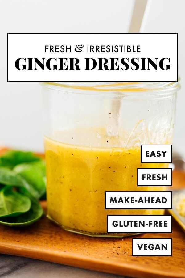 a glass jar filled with ginger dressing on top of a wooden cutting board next to green leaves