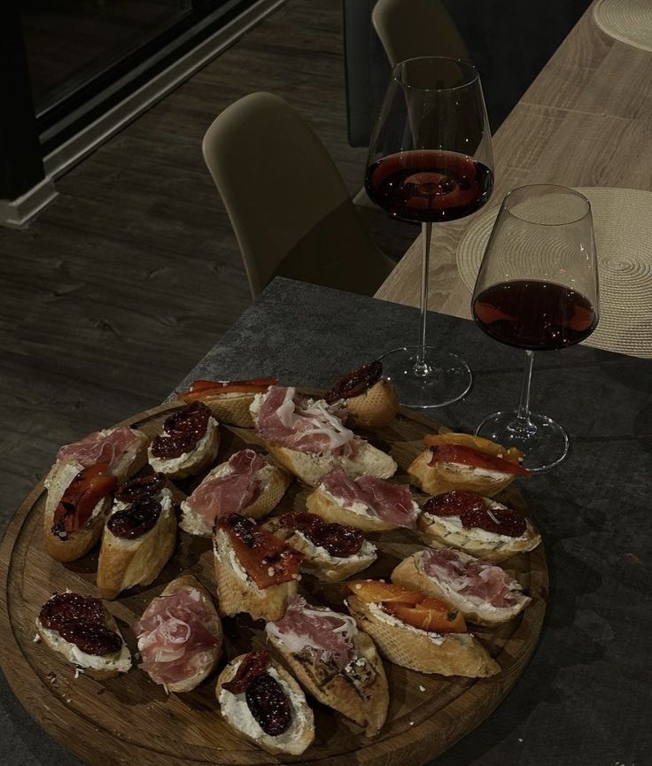 a wooden plate topped with lots of food next to wine glasses