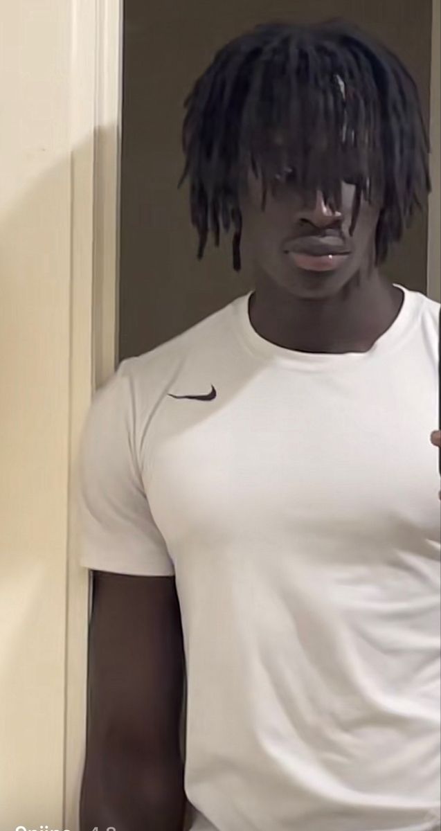 a man with dreadlocks standing in front of a door wearing a white shirt