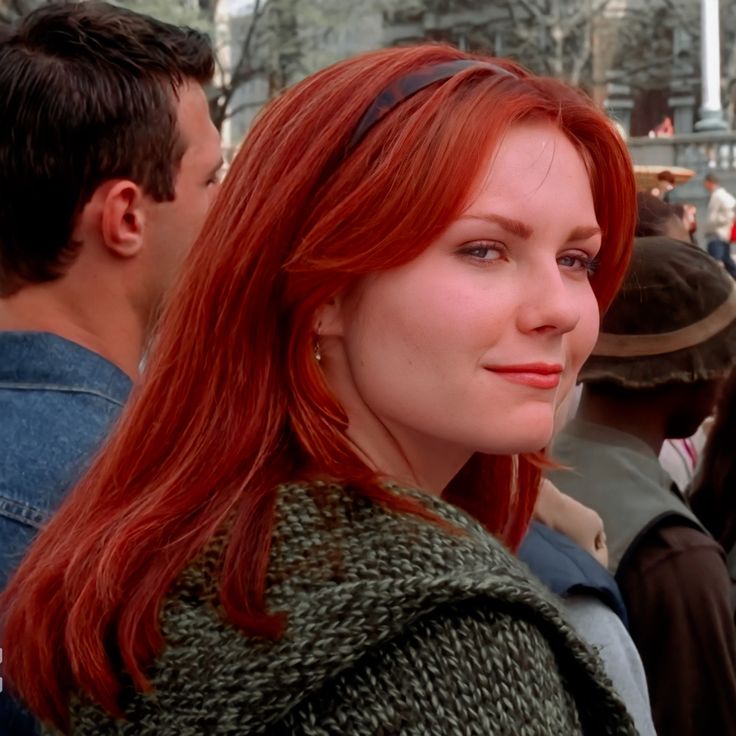 a woman with long red hair standing in front of a group of people and looking at the camera