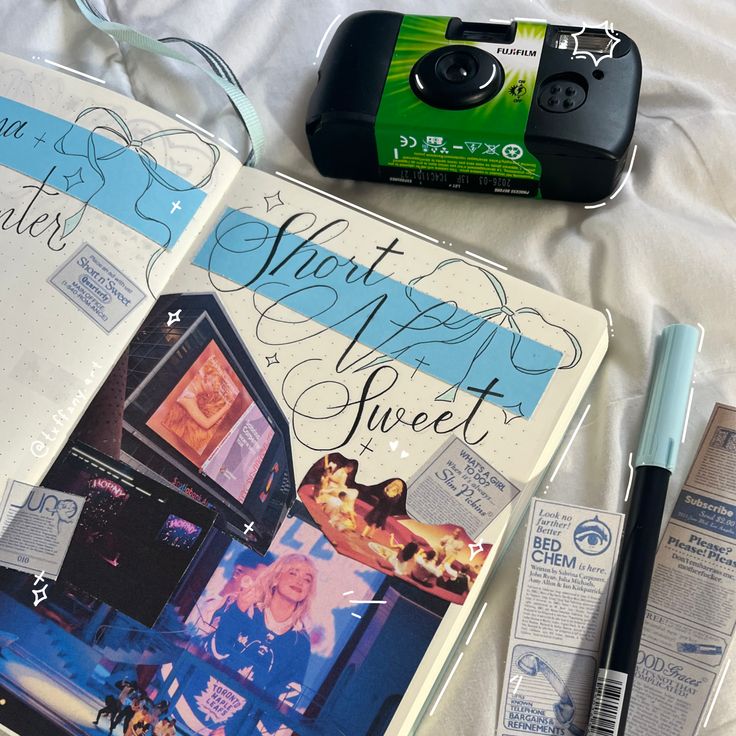 an open book sitting on top of a bed next to a cell phone and pen