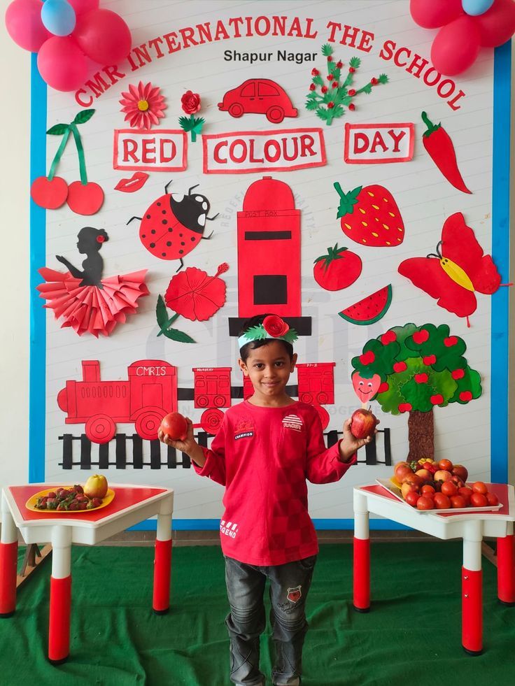 a young boy standing in front of a school bulletin board decorated with fruits and vegetables