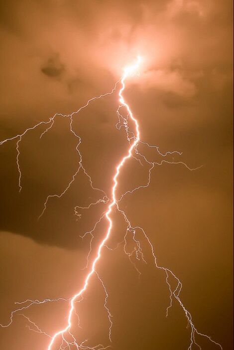 a lightning bolt is seen in the sky during a storm at night with dark clouds and orange hues