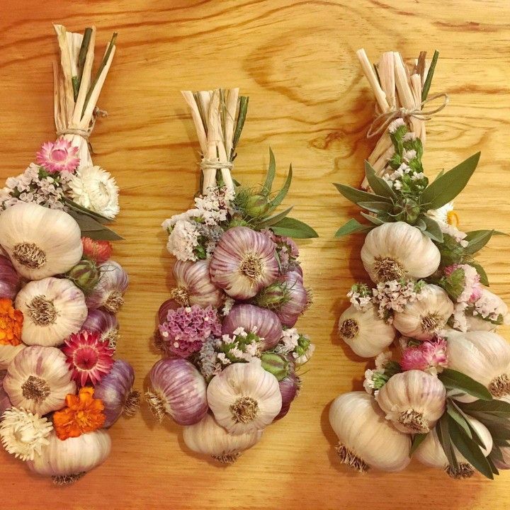 three bunches of garlic are arranged on a table with flowers and herbs in them