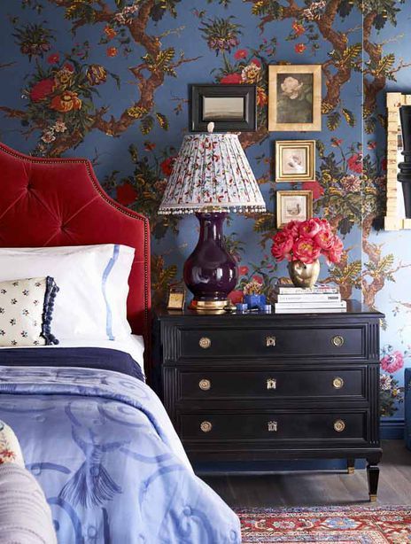 a bedroom decorated in blue and red with flowers on the wall, bed linens, lamps, and pictures