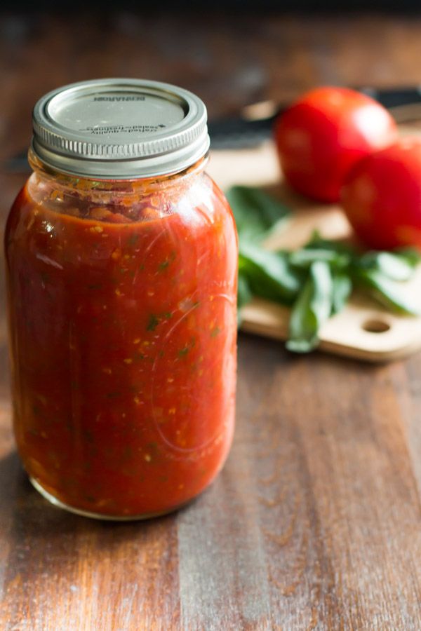 a jar of tomato sauce sitting on top of a wooden table next to tomatoes and basil