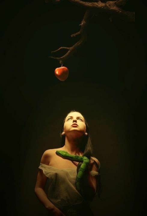 a woman standing in front of a tree with an apple hanging from it