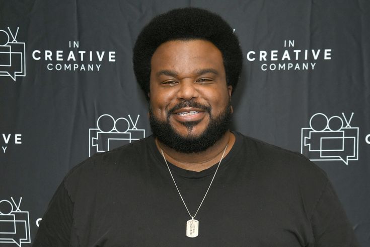 a man with a beard standing in front of a black backdrop and smiling at the camera