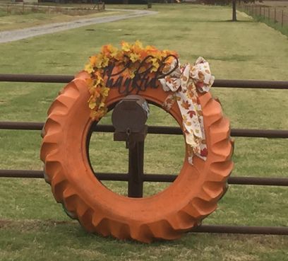 an orange wreath on top of a fence in front of a grassy field with trees