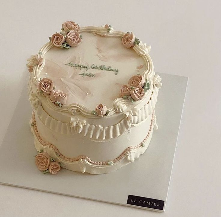 a white cake with pink roses on it sitting on top of a table next to a book