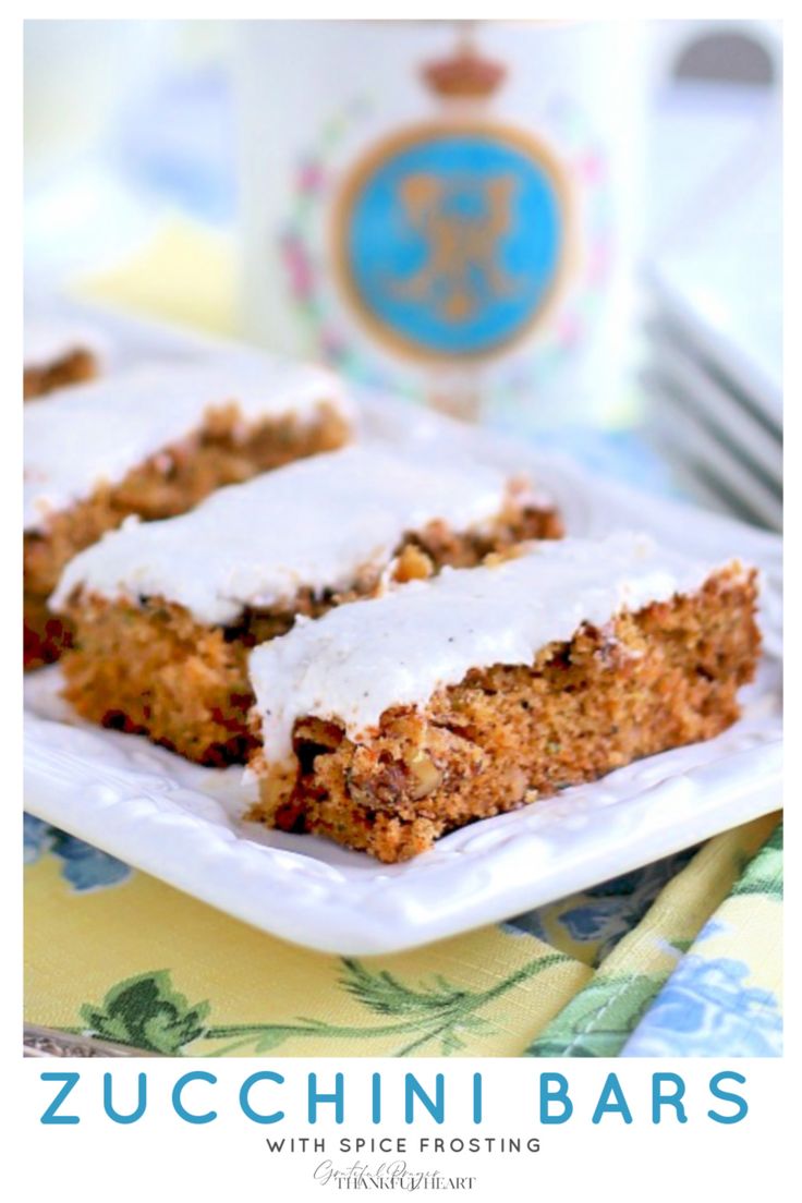 two slices of zucchini bars with white frosting on a plate next to a bottle