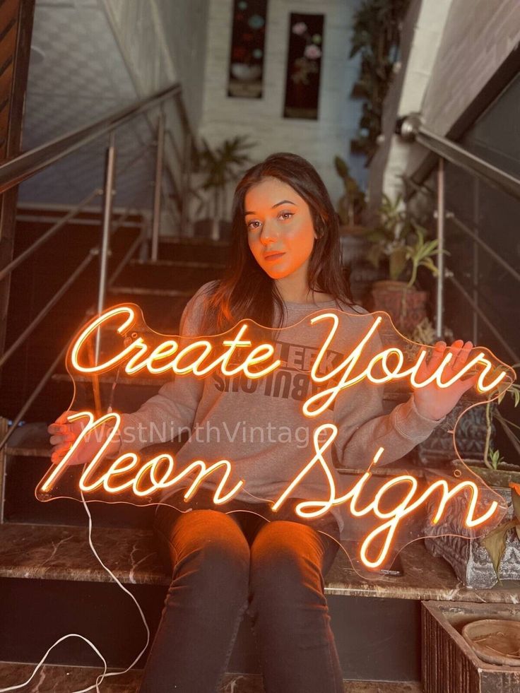 a woman sitting on the steps holding up a neon sign that reads create your moon sign