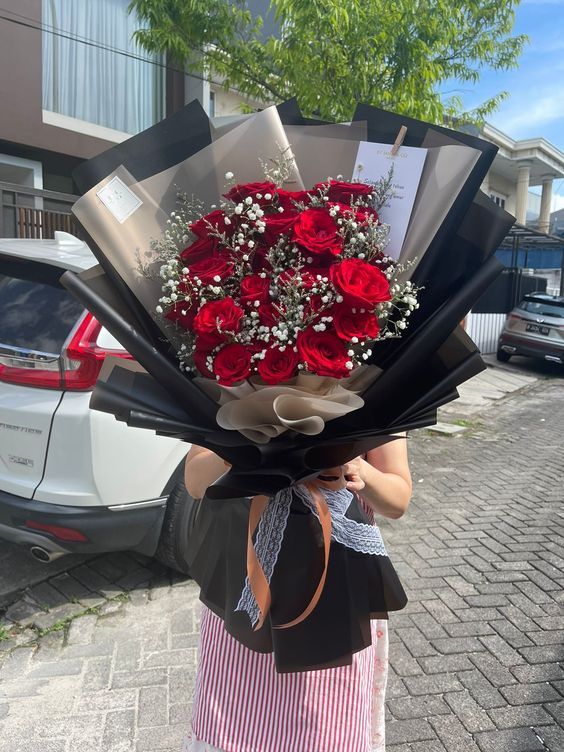 a woman holding a bouquet of red roses in front of her face on the street