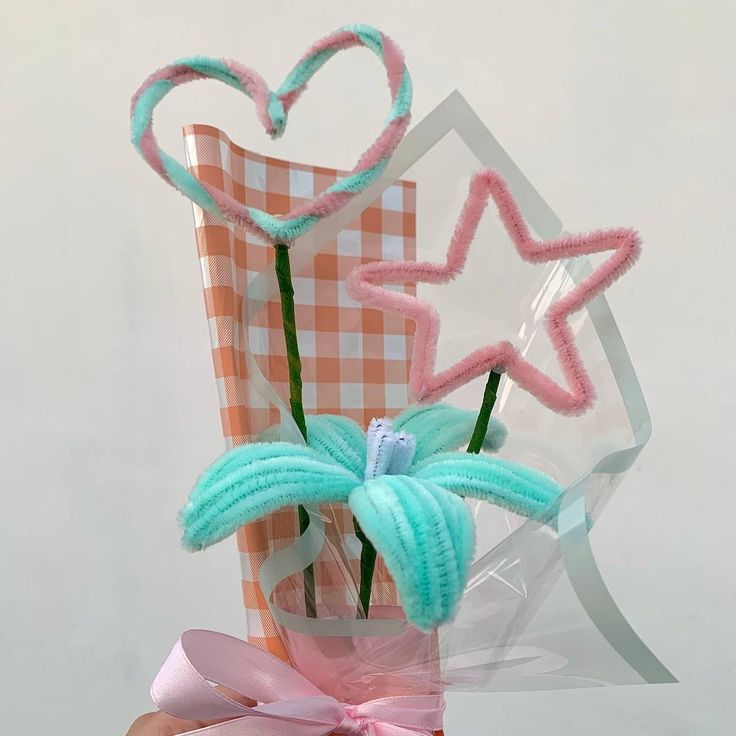 a vase filled with pink and blue flowers next to a heart shaped decoration on top of a checkered table cloth