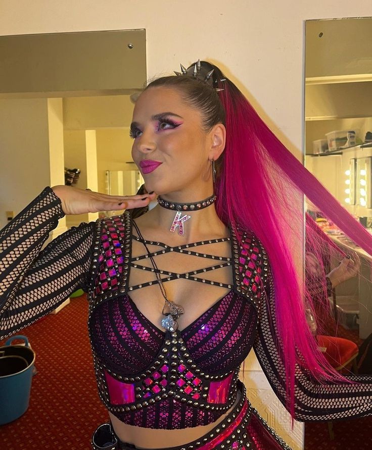 a woman with pink hair wearing a purple outfit and posing in front of a mirror