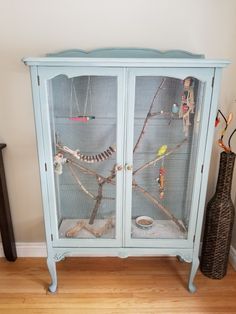 a blue cabinet with birds in it on top of a hard wood floor next to a vase