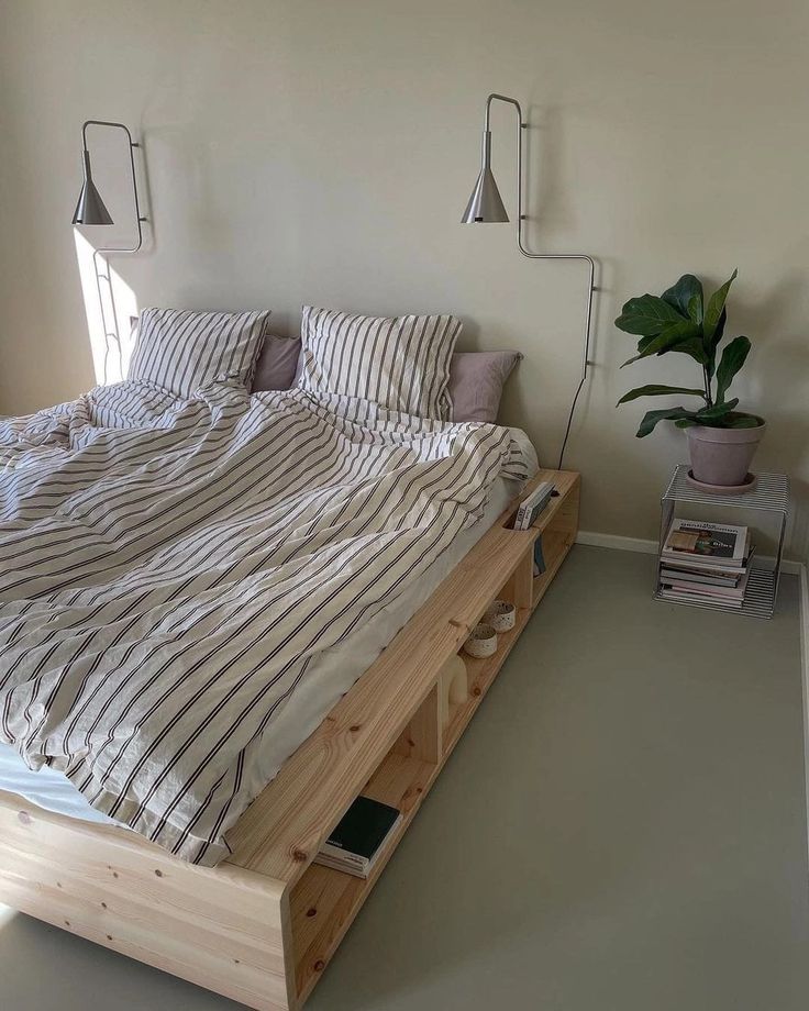 a bed that is made up with some pillows and blankets on top of it, next to a potted plant