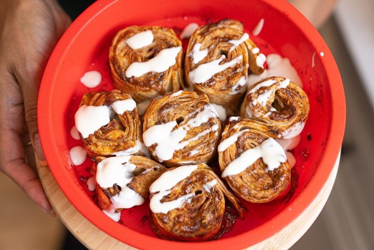 a red bowl filled with cinnamon rolls covered in icing