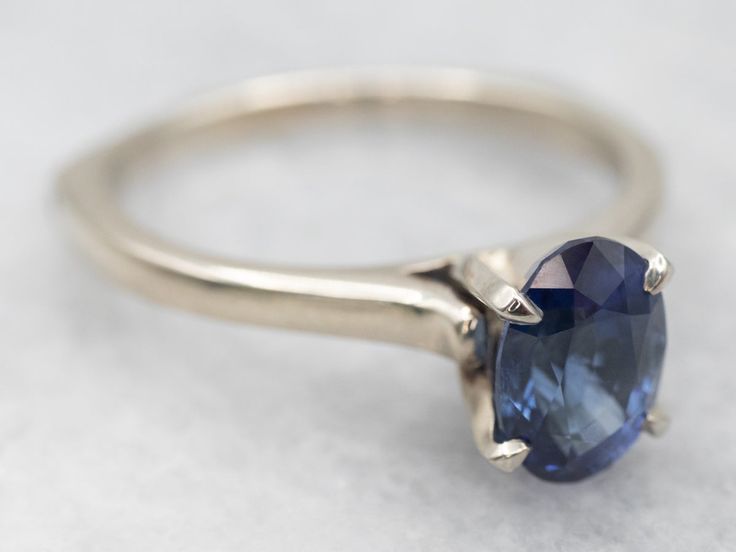 This is a well-proportioned ring, classic and sophisticated. The brightly polished sides have a great heft to them, and this is comfortable on the finger, with a rich feel. We've set the center with a bright blue Ceylon sapphire that has glittering navy and cobalt highlights and plenty of sparkles.Metal: 14K White GoldGem: Sapphire 1.85 CaratsGem Measurements: 6.2 x 8.6 mm, OvalAccents: Diamond .01 Carats, J in Color, I in ClarityRing Size: 9Marks: "14Kt" Stamped on the inside band Classic Oval Sapphire Ring, Classic Sapphire Birthstone Ring With Gemstone, Timeless Sapphire Ring With Prong Setting, Classic Sapphire Birthstone Ring, Timeless Polished Sapphire Ring, Classic Sapphire Halo Ring, Timeless Sapphire Ring With Brilliant Cut, Timeless Sapphire Birthstone Ring For Anniversary, Timeless Sapphire Anniversary Ring