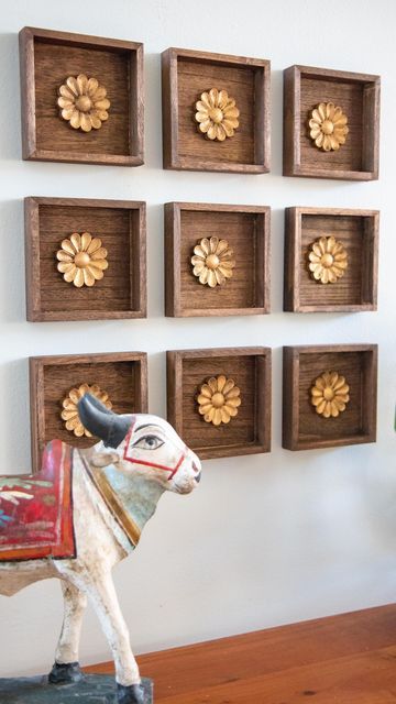 a cow statue sitting on top of a wooden table in front of some wall hangings