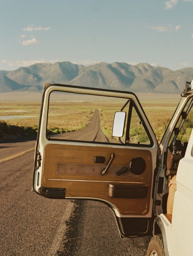 the driver's door is open on an empty road with mountains in the background