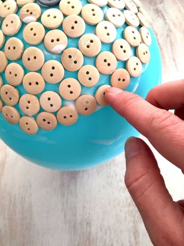 a blue bowl filled with lots of buttons on top of a white wooden table next to a person's finger