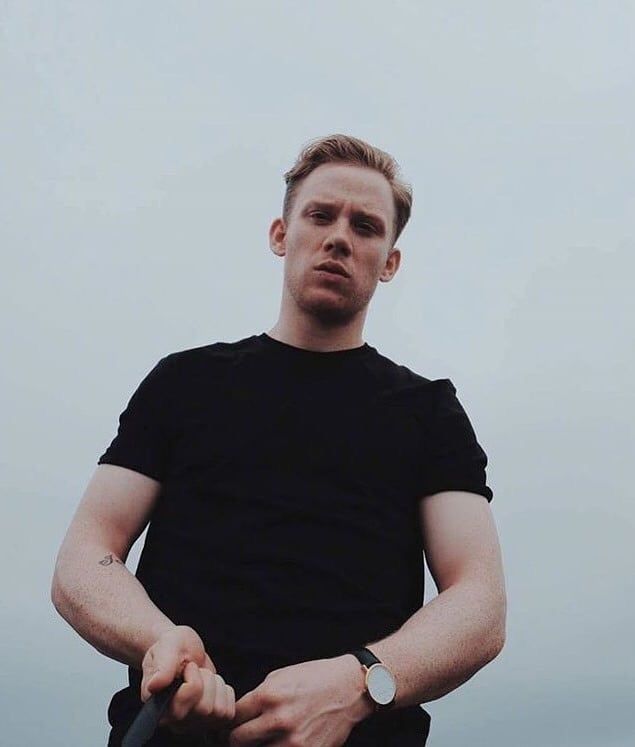 a man standing in front of the ocean with his hands on his hips and looking at the camera