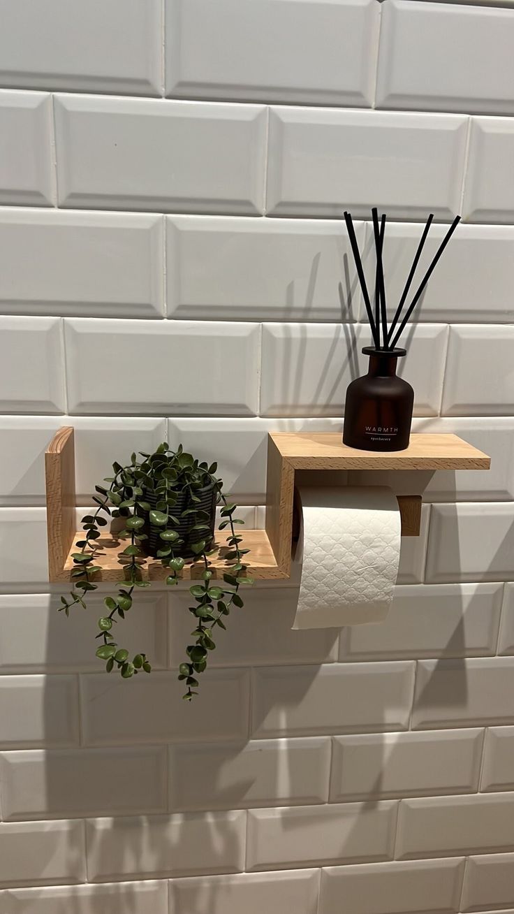 a white brick wall with two wooden shelves holding plants and toilet paper