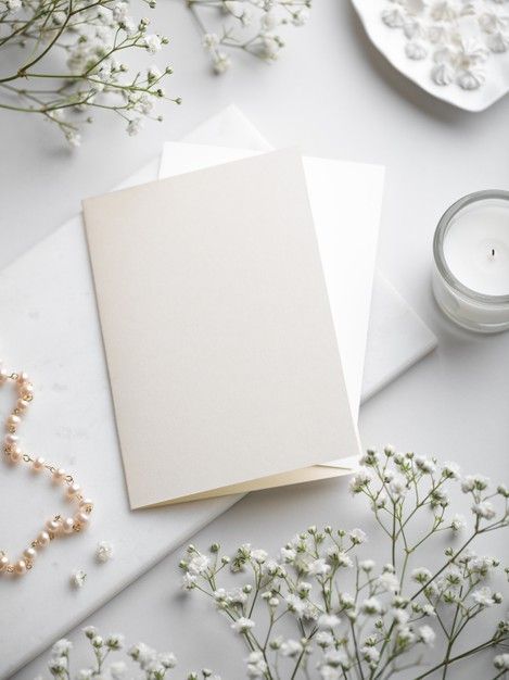 two blank cards sitting on top of a table next to some flowers and pearls with a candle