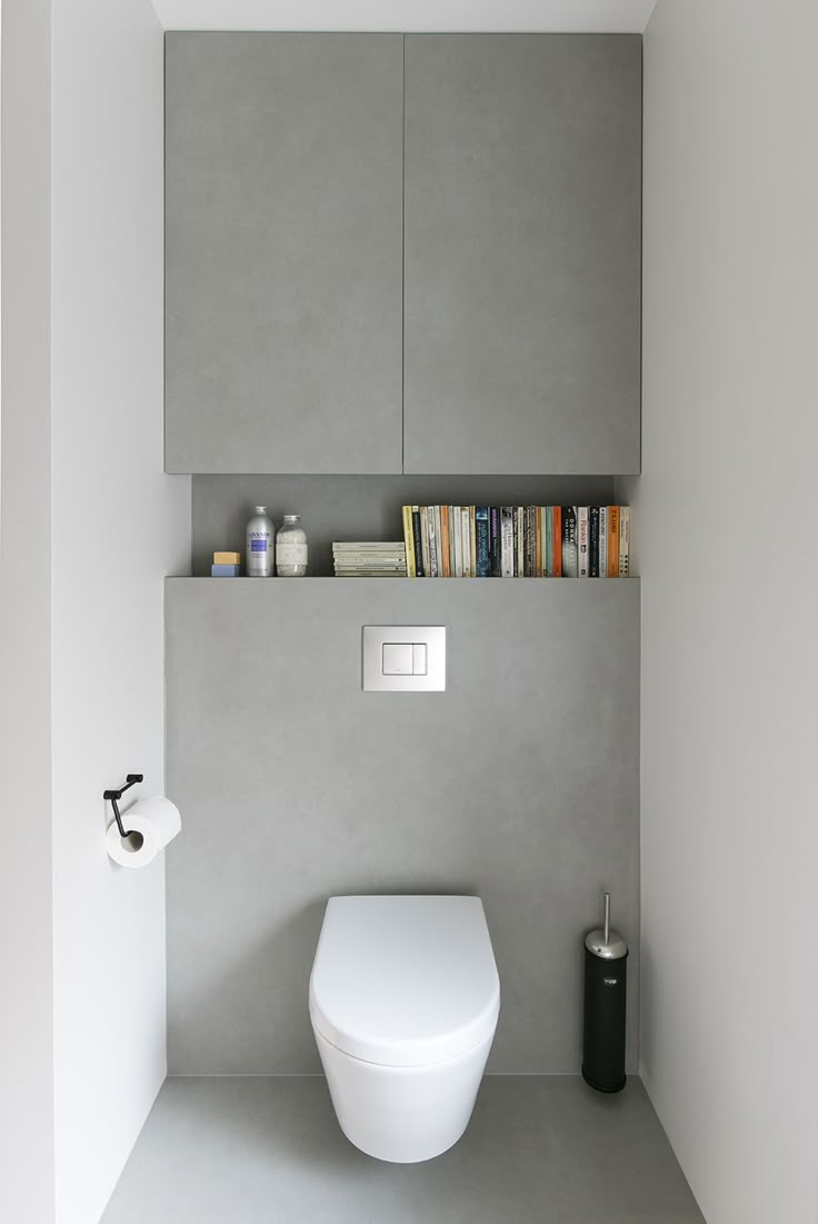 a white toilet sitting in a bathroom next to a wall mounted book shelf filled with books