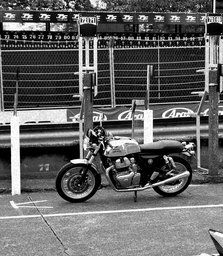 a black and white photo of a motorcycle parked in front of a fenced area