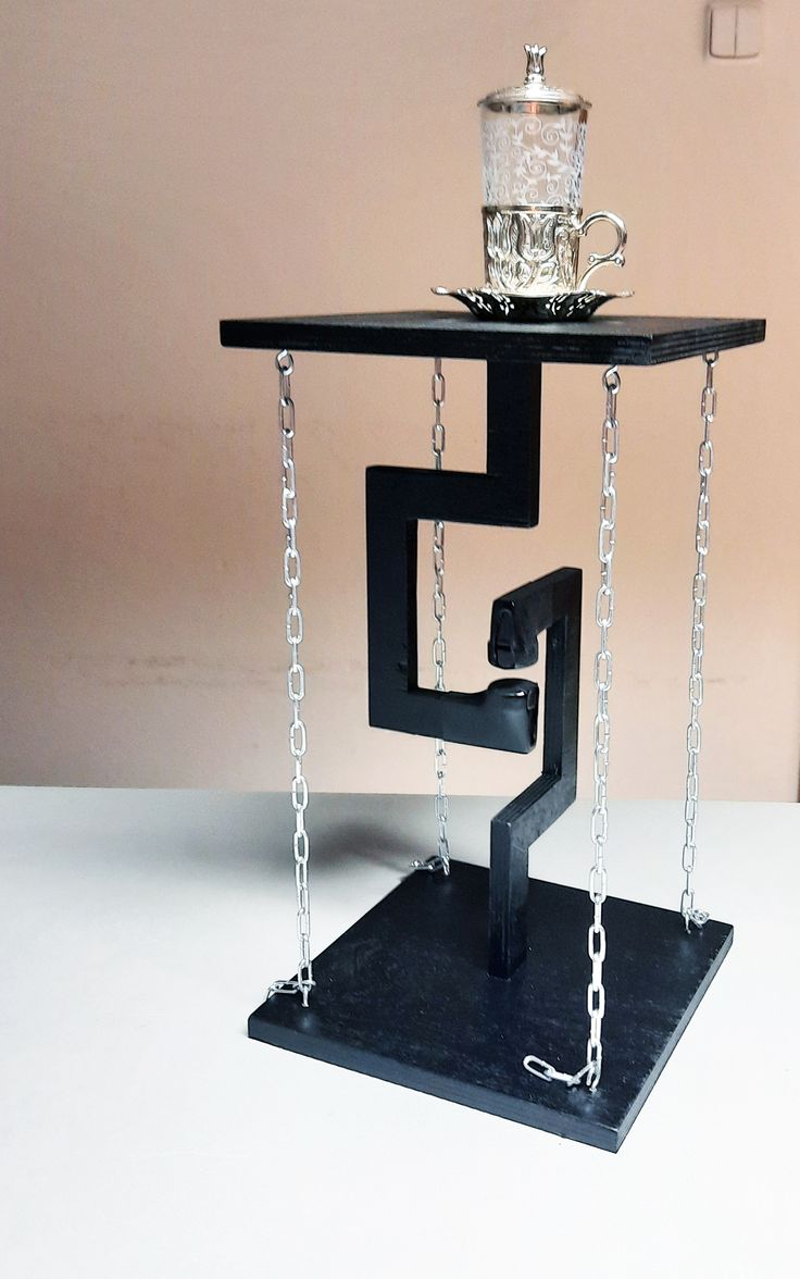 a glass teapot sitting on top of a black stand with chains hanging from it