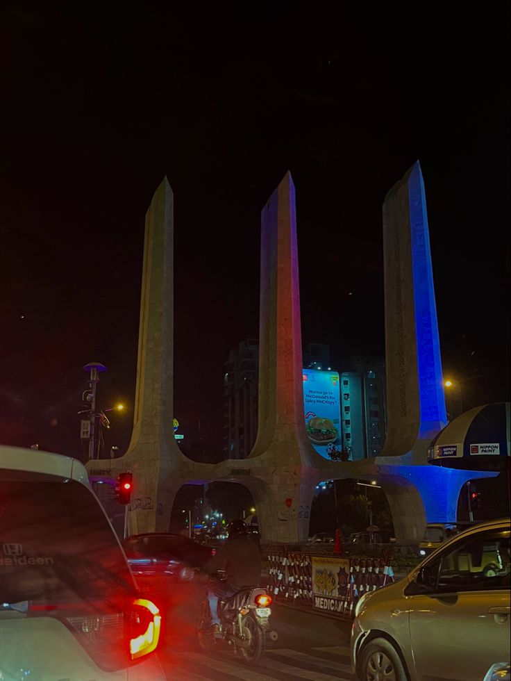 cars driving down the road at night with tall buildings in the background and traffic lights on both sides