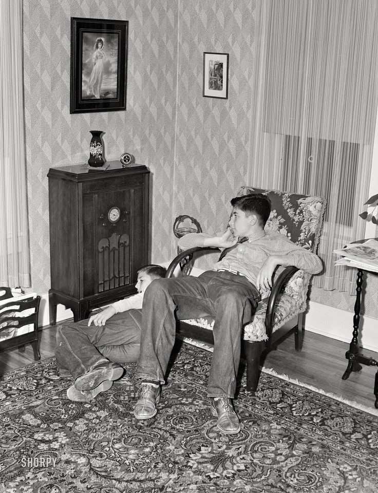 black and white photograph of man sitting in chair with another person laying on the floor