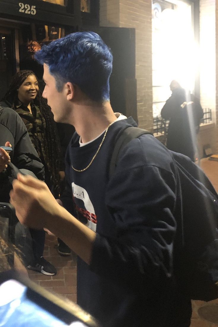 a man with blue hair is looking at his cell phone while people stand in the background