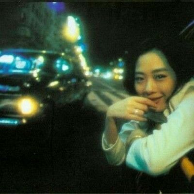 a woman sitting in the drivers seat of a car on a city street at night