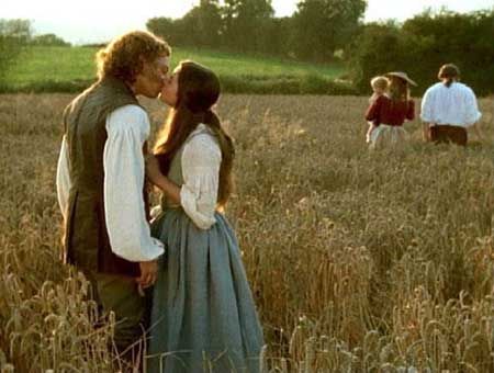 a man and woman kissing in the middle of a field with other people standing around