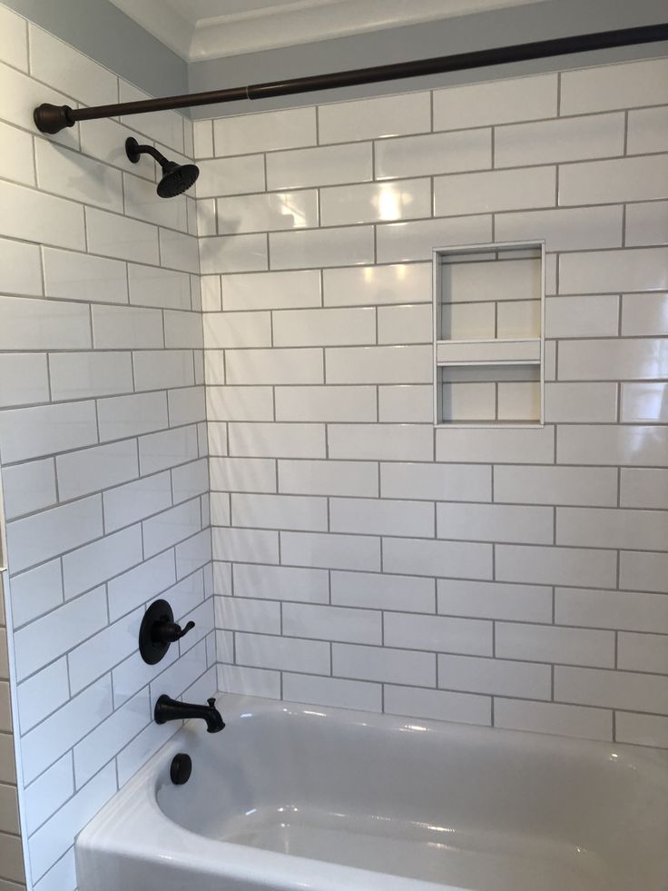 a bathroom with white subway tile and black faucet shower head in the corner