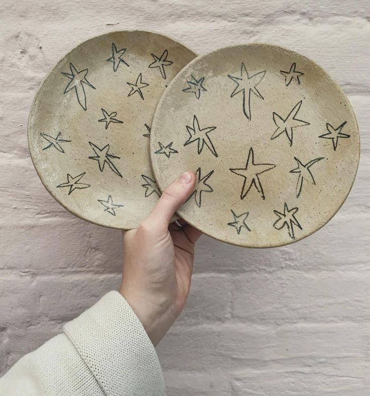 two plates with stars painted on them in front of a white brick wall, one being held up by a person's hand